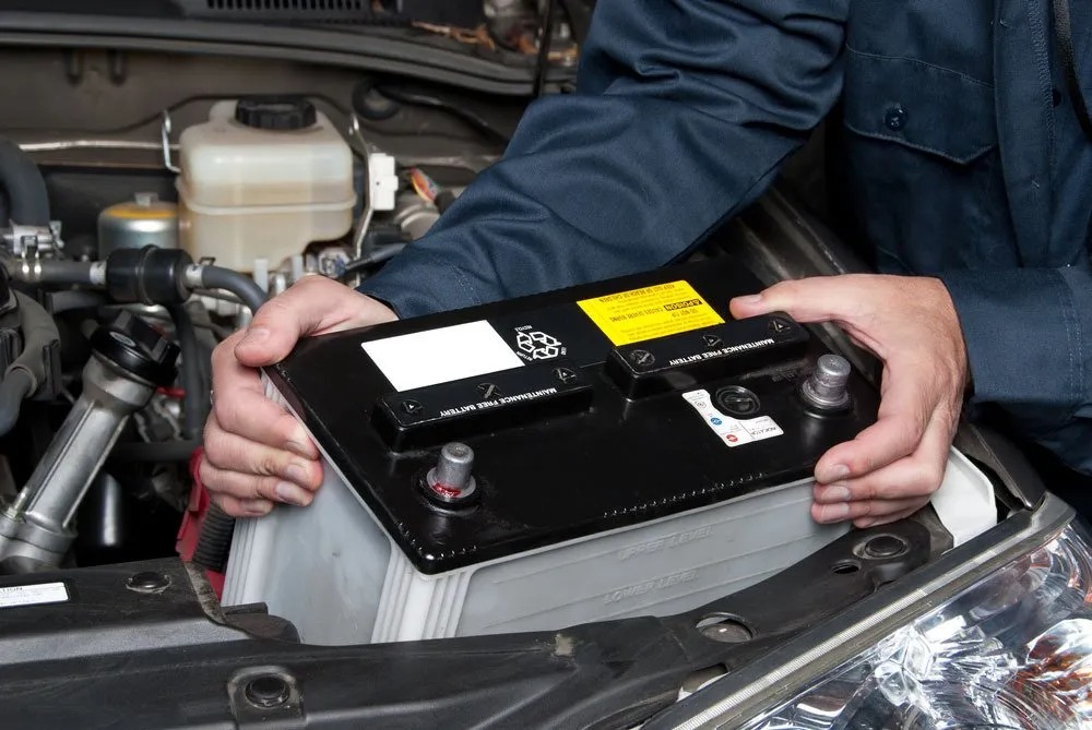 Mechanic replacing a car battery under the bonnet in Boonah